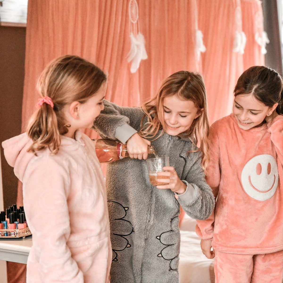 Drie meisjes in roze pyjama lachen samen op een slaapfeestje