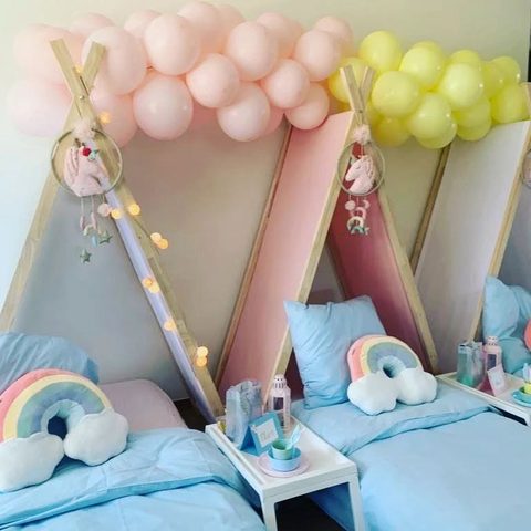Bedjes met regenboogkussens en een ballonnenboog